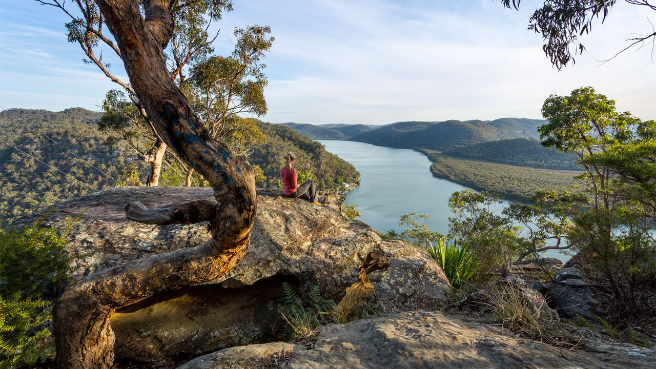 Female sitting on a large rock relaxing in afternoon dappled light the Australian bushland with views over the river